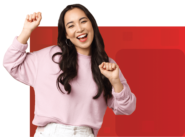 A woman in a light pink sweatshirt dances with raised arms against a vibrant red background, expressing joy and enthusiasm in a lively workspace moment.